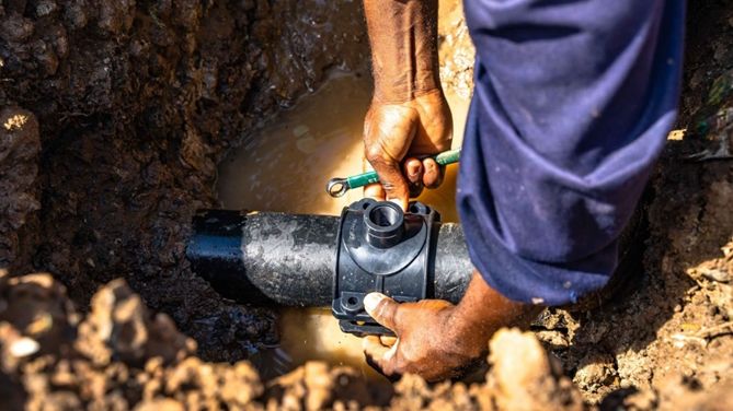Ein Mitarbeiter eines Versorgungsunternehmens schraubt eine Armatur an ein Rohr, um ein Haus an das Trinkwassernetz anzuschließen.