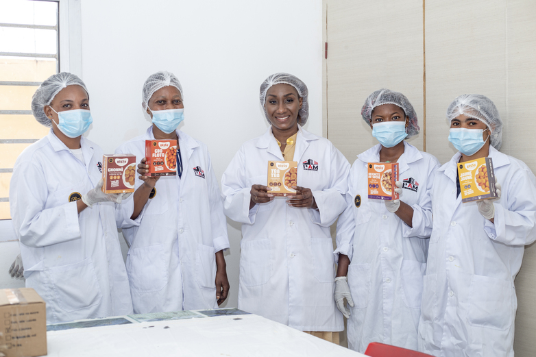 Fünf Frauen in weißer Arbeitsschutzkleidung halten ivorische Lebensmittelprodukte hoch.
