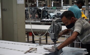 Ein Fabrikarbeiter schneidet mit einer Maschine Textilien zurecht.