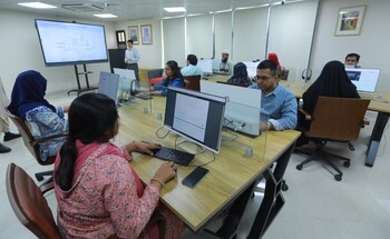Mehrere Personen sitzen in einem Raum und arbeiten für sich jeweils an einem Computer.