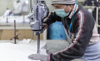 Ein Textilarbeiter trägt eine Schutzmaske und bearbeitet ein Möbelstück.