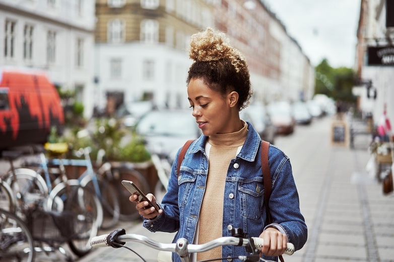 Eine Frau steht neben ihrem Fahrrad und schaut auf ihr Smartphone.