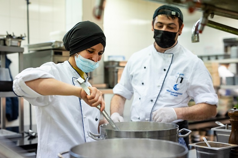 Eine THAMM-Projektteilnehmerin, die eine Ausbildung als Köchin macht und ihr Kollege arbeiten am Kochtopf in einer Küche. © GIZ/Hinrich Franck