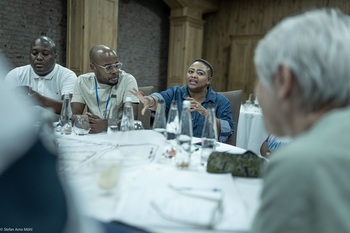 Mehrere Personen sitzen diskutierend an einem Tisch, auf dem Pläne und Karten liegen. 