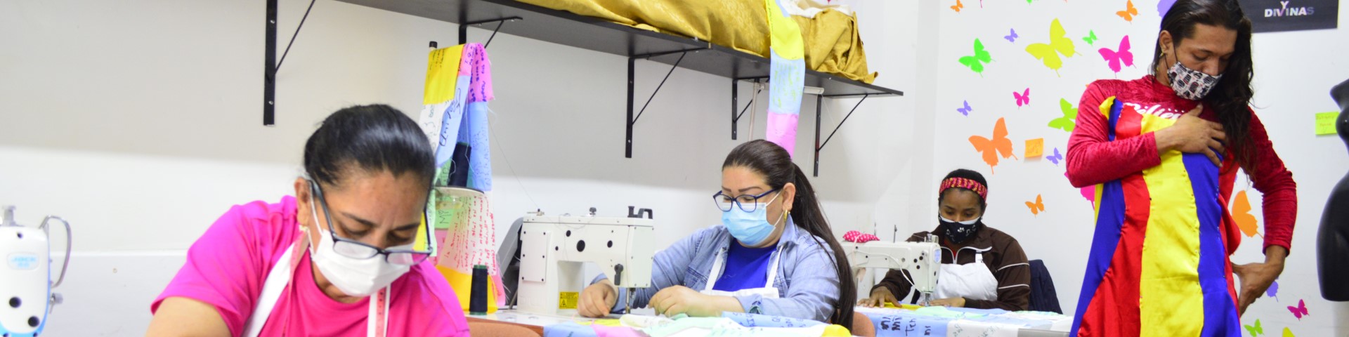 Frauen arbeiten an Nähmaschinen, eine Person probiert ein Kleid an.