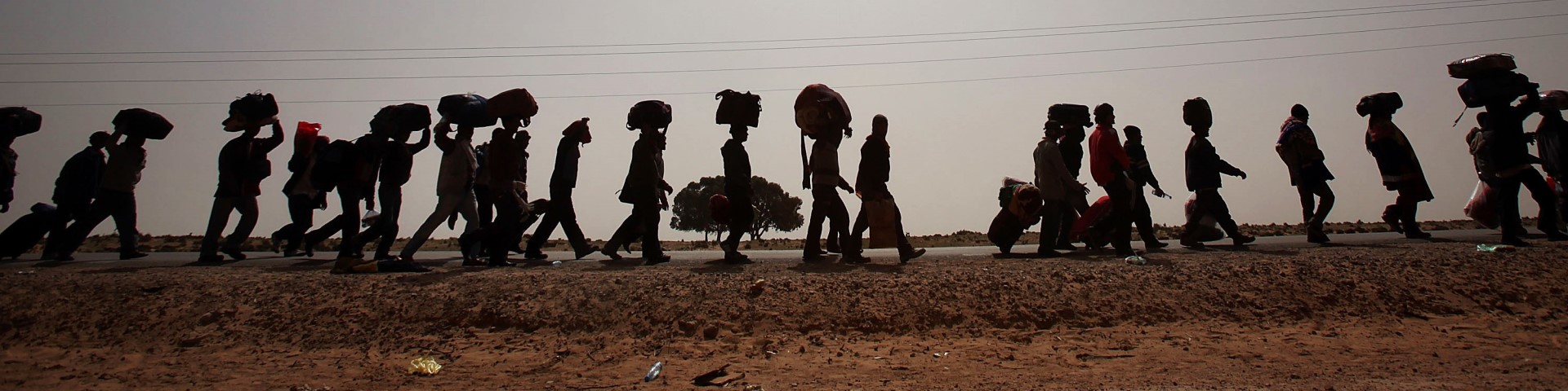 Eine Gruppe von Menschen, die in der Wüste laufen und schweres Gepäck tragen.