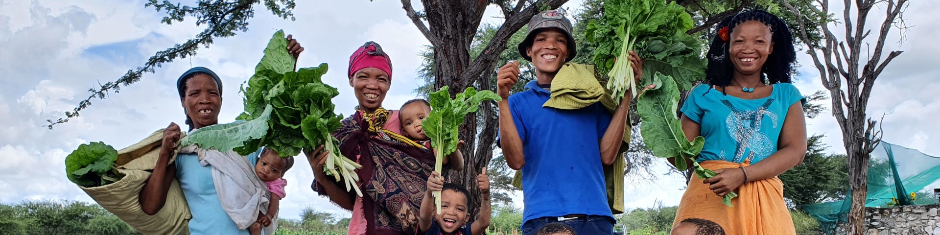 Vier Landwirt*innen stehen mit ihren Kindern und ihrer Ernte auf ihrem Gemeinschaftsfeld