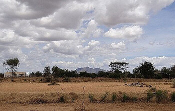 Landschaftsaufnahme aus Karamoja im Nordosten Ugandas: Wolken am Himmel, vorne trockener Boden und einzelne Sträucher, im Hintergrund Bäume und ein Gebirgszug. © Heike Wintershoff/GIZ