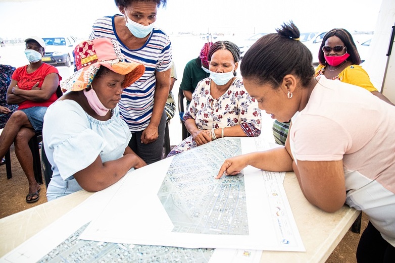 Vier Frauen schauen auf einen Plan der Donkerhoek-Siedlung in Mariental und eine von ihnen zeigt auf eine Stelle.
