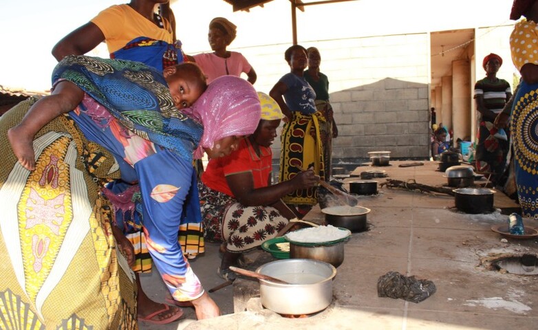 Eine Gruppe von Frauen bereitet Essen auf einem improvisierten Herd mit vielen Kochfeldern zu.