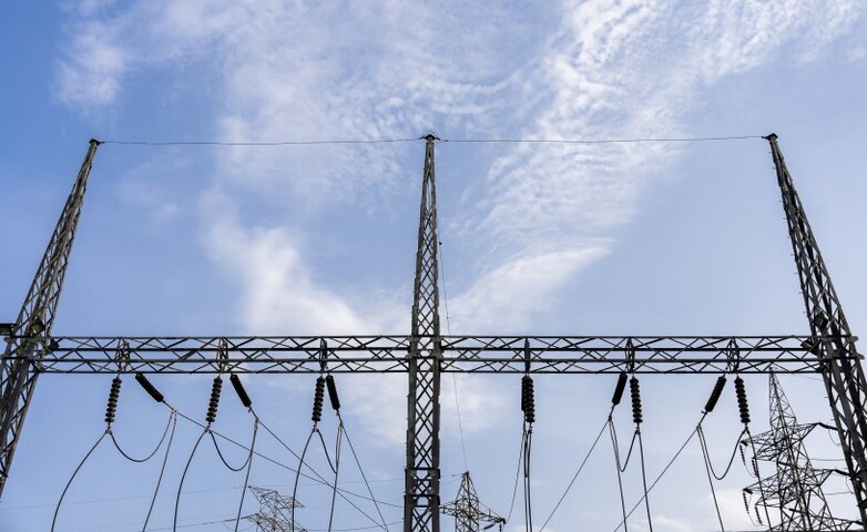 Hochspannungsleitungen und Strommasten erstrecken sich durch die Landschaft und befördern Strom über längere Entfernungen.