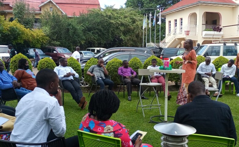 Eine Frau hält im Freien vor einem Rednerpult eine Ansprache an eine aufmerksame Gruppe von sitzenden Menschen.