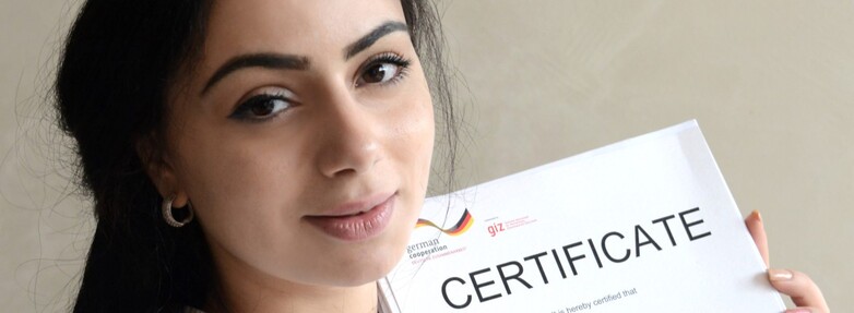 Eine junge Frau hält lächelnd ein Zertifikat.
