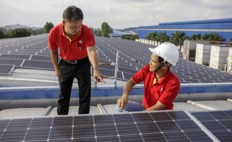 Zwei Solartechniker arbeiten auf einem Dach an einer Solaranlage in Vietnam