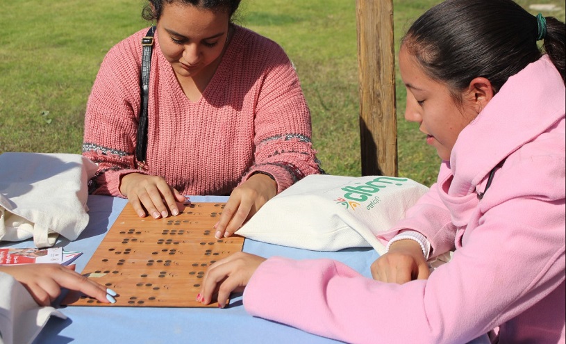 Drei junge Frauen mit geschlossenen Augen berühren mit den Fingern eine Holzbrett mit Braille-Schrift.