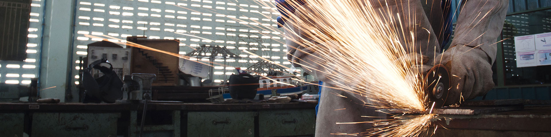 A person operates a grinder in a workshop and sparks are coming out of it.