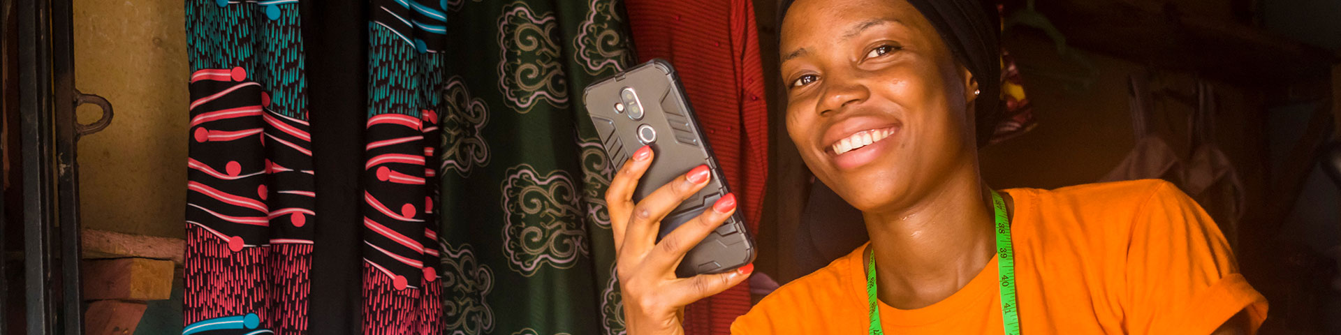 A smiling young African woman holds a mobile phone in her hand