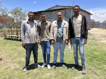 Four men are standing in front of a farm.