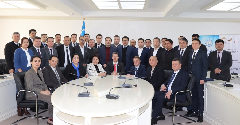 A group photo with many men and some women in suits gathered in a semicircle around a round table in a Uzbek administrative court.
