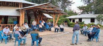 Mujeres y hombres sentados al aire libre en sillas azules en el centro de formación para la adaptación escuchando una conferencia.