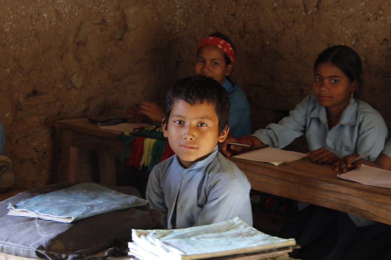 Three Nepalese children in school uniform sitting in rows at desks.