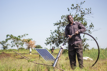 Un homme se tient dans un champ, tenant à la main un tuyau d'irrigation alimenté par l'énergie solaire.