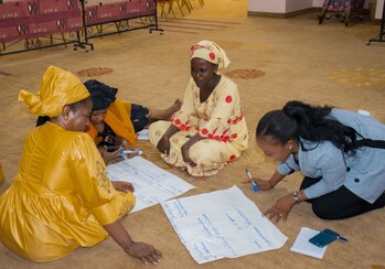 Four Malian women sit on the floor, writing on posters during a training workshop on gender sensitivity.