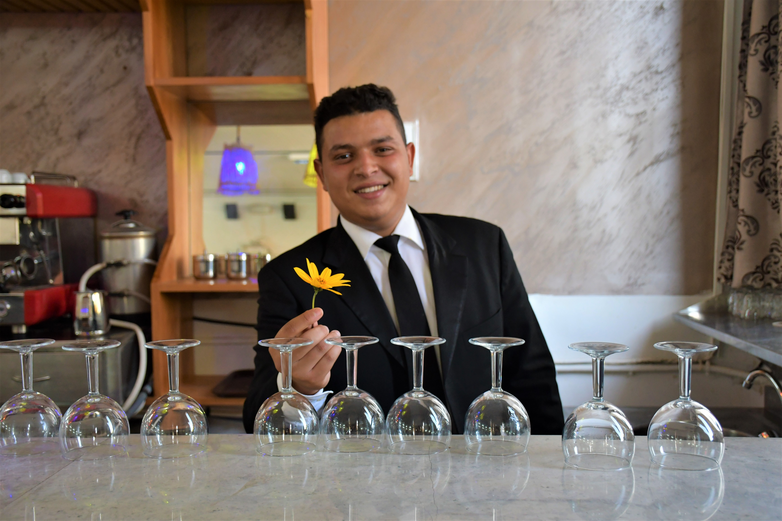 A young man stands behind a restaurant counter holding a flower.