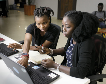 Two women sit at laptops in a Nigerian innovation centre and discuss the task in hand. © GIZ / Thomas Imo