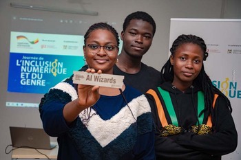A young woman smiles and holds a sign reading ‘AI Wizards’ at the ideas competition for young digital entrepreneurs. Two more young people stand behind her. Copyright: GIZ