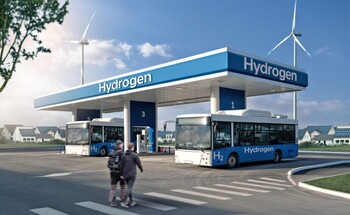 Two people walking towards a hydrogen station with two parked busses.