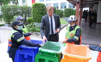 A man in a suit engages in a discussion with four workers in front of three colorful rubbish containers.