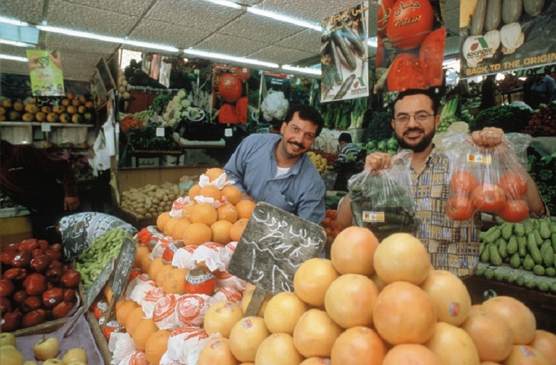 Two men selling fruit and vegetables at a market stand.