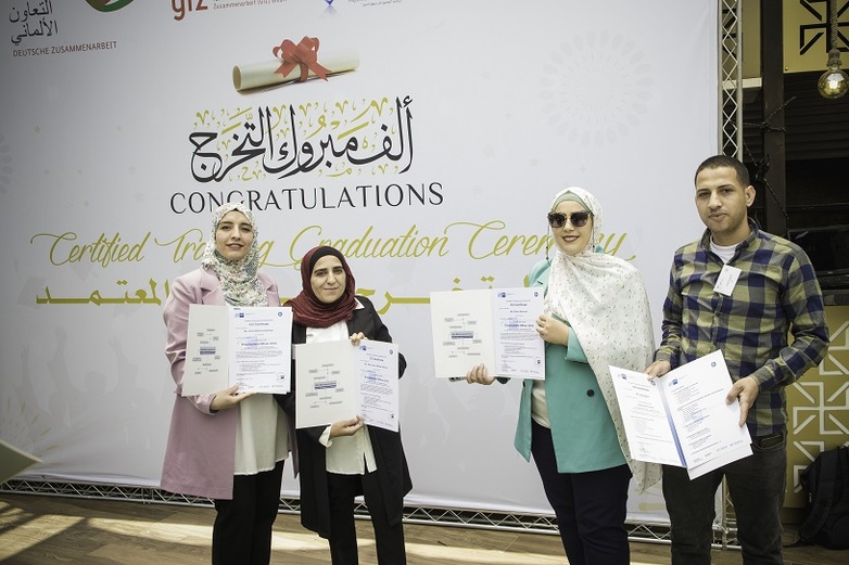 Four people show their certificates to the camera at the PALM graduation ceremony for recruitment advisors. Copyright: GIZ / Ameen Saeb.