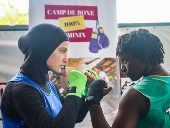 Two women face each other with clenched fists while boxing.