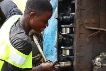 A trainee mechanic works on lorry parts.