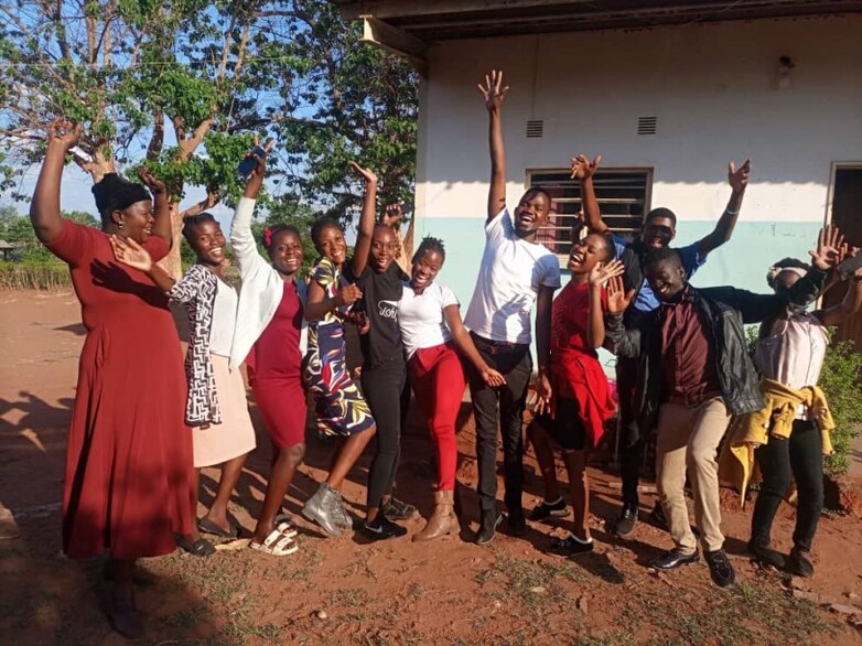 Eleven peer educators laugh, cheer and raise their arms in the air in Kasempa.