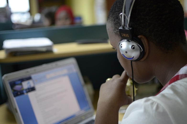 A school child is sitting in front of a laptop with headphones.