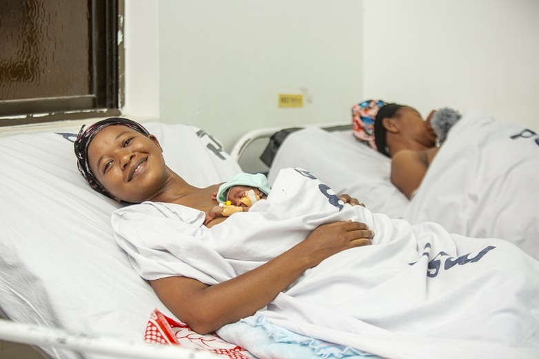 A smiling mother lies with her newborn in a hospital bed.