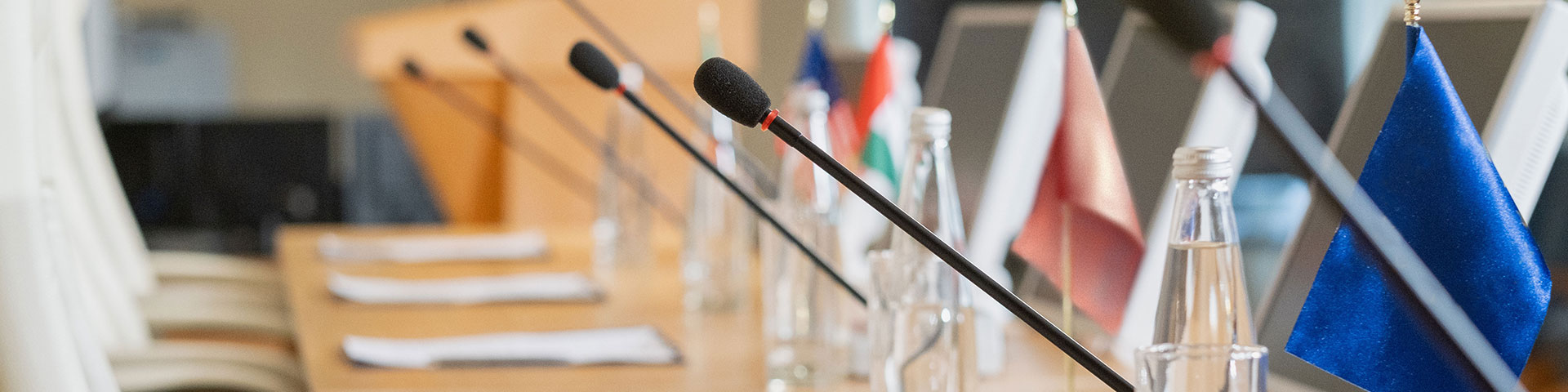 A row of microphones and small flags on a conference table.
