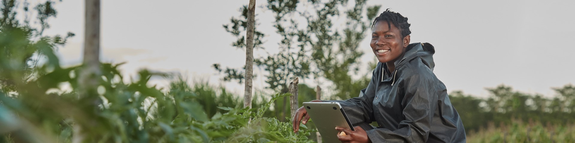 A person squats in a field holding a tablet.