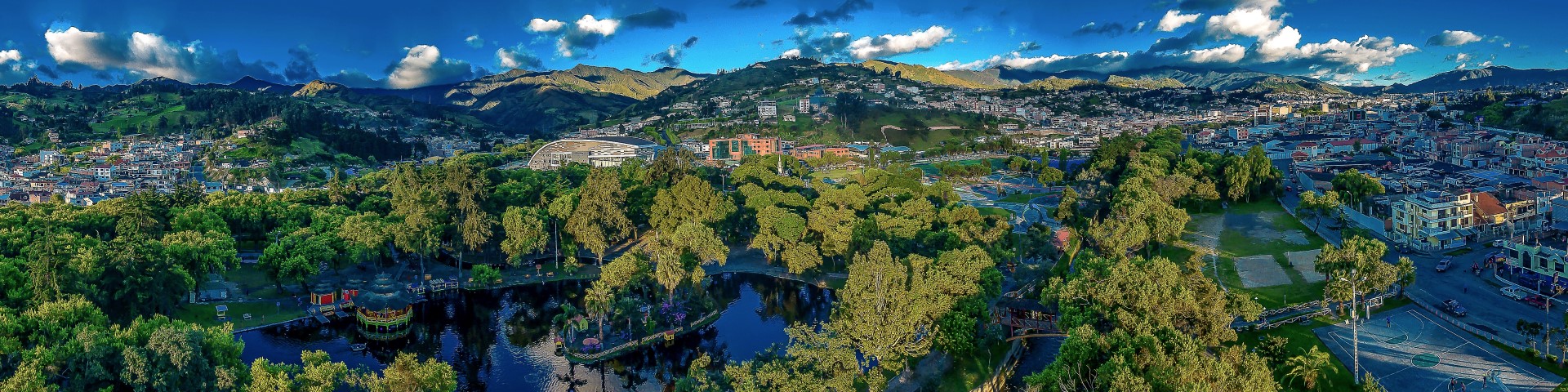 Panoramic image of a park surrounded by a green city and a hilly landscape.