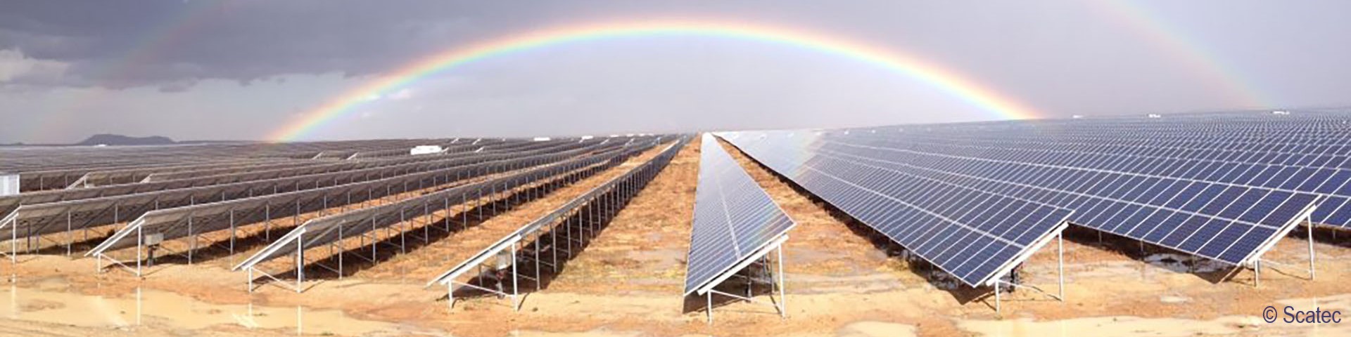 A large number of solar panels standing in rows in a field. There are two rainbows above them. Copyright: Scatec