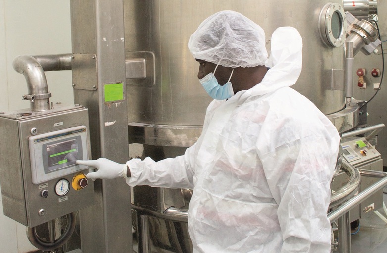 Un technicien en tenue de protection est entrain de sécher des granulés ou poudres dans l’usine pharmaceutique.