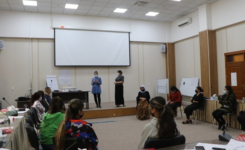 Two women speak to a circle of participants at a training session