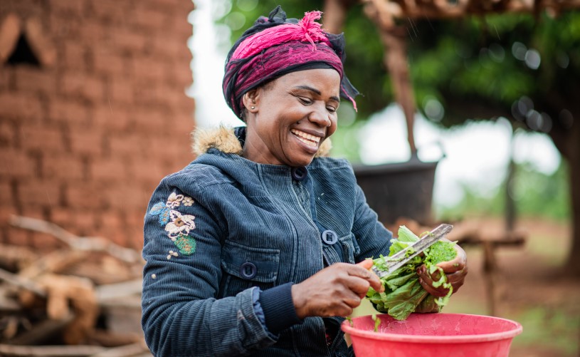 A woman processes vegetables and smiles.