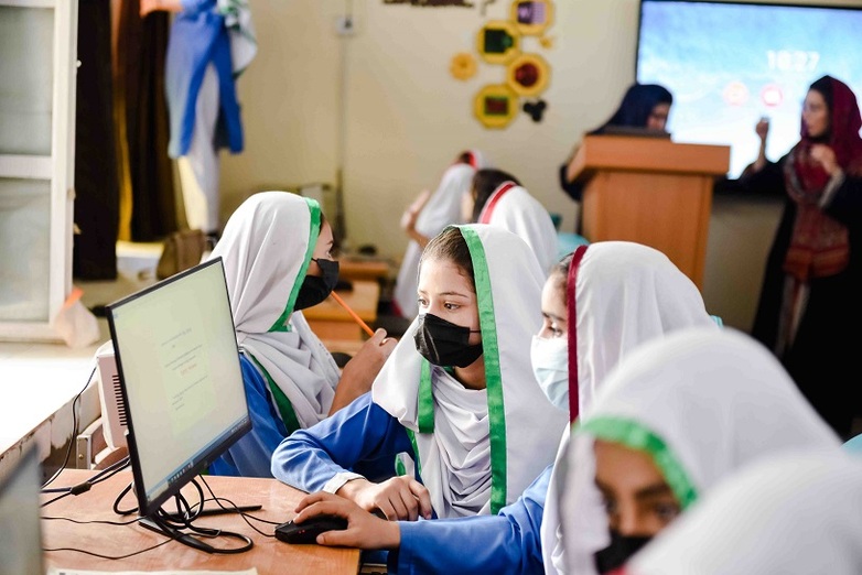 Young women and girls sitting in front of a computer screen and reading something on it.