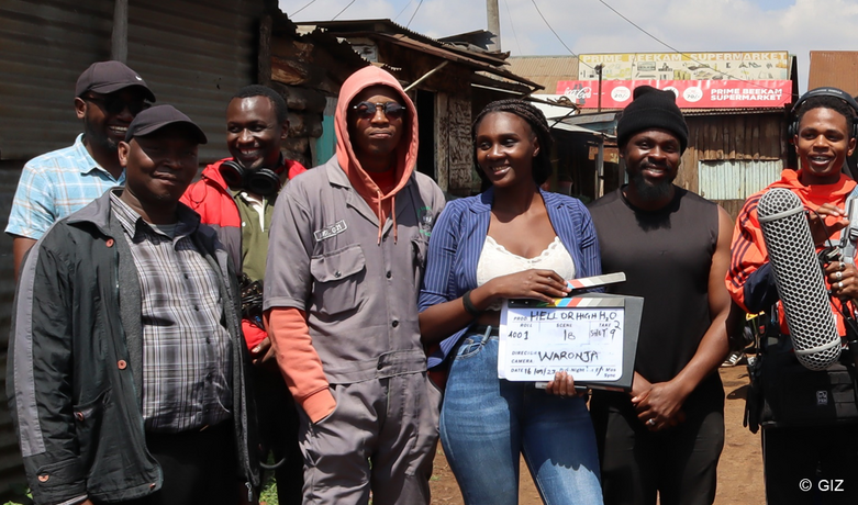 Seven people smiling into the camera. One of them is holding a clapperboard.