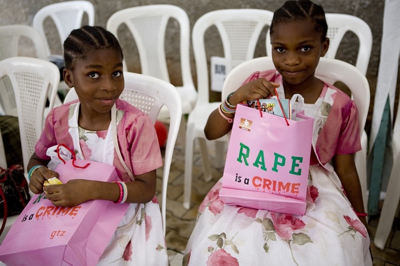 Two young girls hold gift bags printed with the words 'Rape is a Crime'