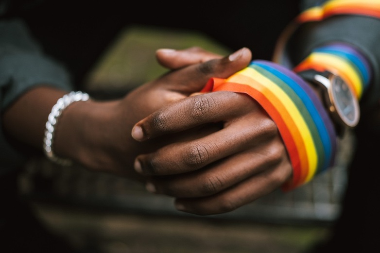 Two clasped hands hold a ribbon in rainbow colours.